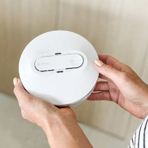 Person holding a white round device with buttons on a neutral background