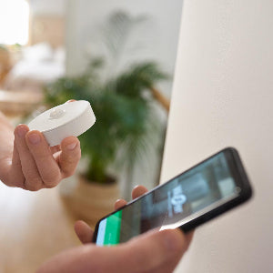 Person holding a white device and a smartphone with a screen displaying an app interface.